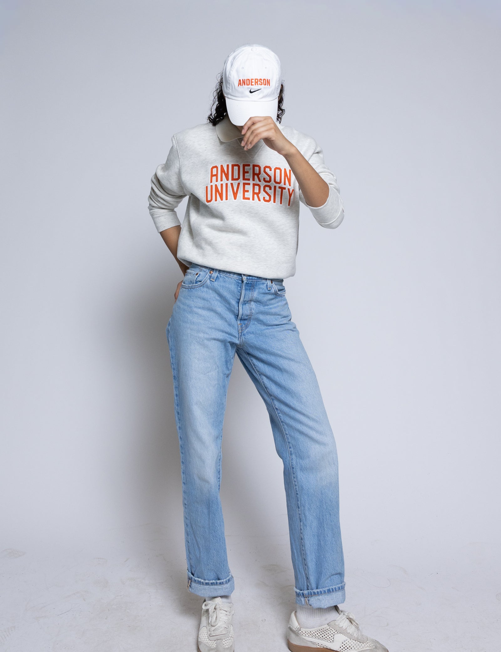 Person wearing an 'Anderson University' sweatshirt with a white cap and light blue jeans on a plain background