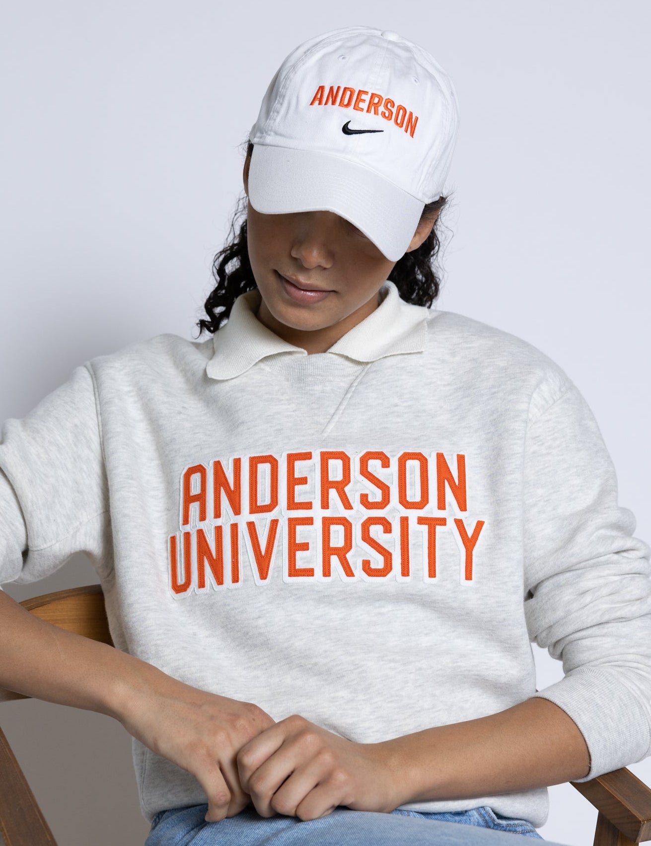 Person wearing Anderson University sweatshirt and cap sitting on a chair.