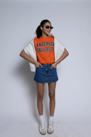 Person wearing an orange 'Anderson University' t-shirt with a white sweater and denim skirt on a plain background